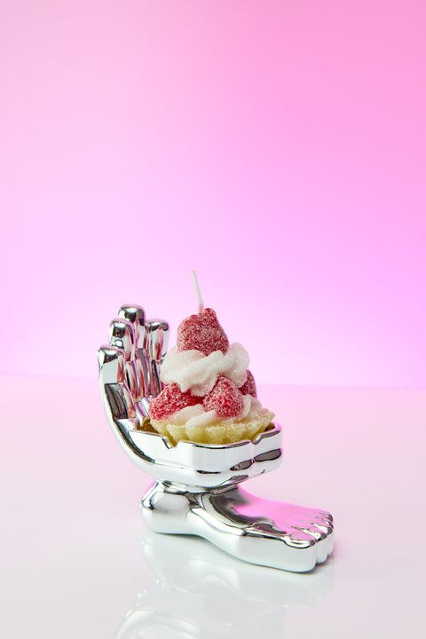 Hand and foot chrome ashtray. Hand is shown palm up with notches to hold cigarette or joint. In the ashtray a Red Sparkle birthday candle sits on display.