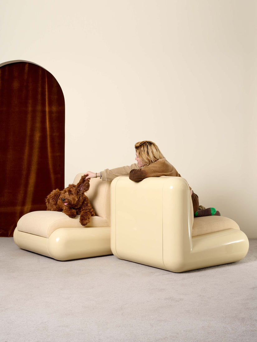 Two cream Uma chairs staggered facing away from each other. Someone sits in the chair that faces away leaning over the back and lifting the air of the brown dog that sits in the opposite chair.