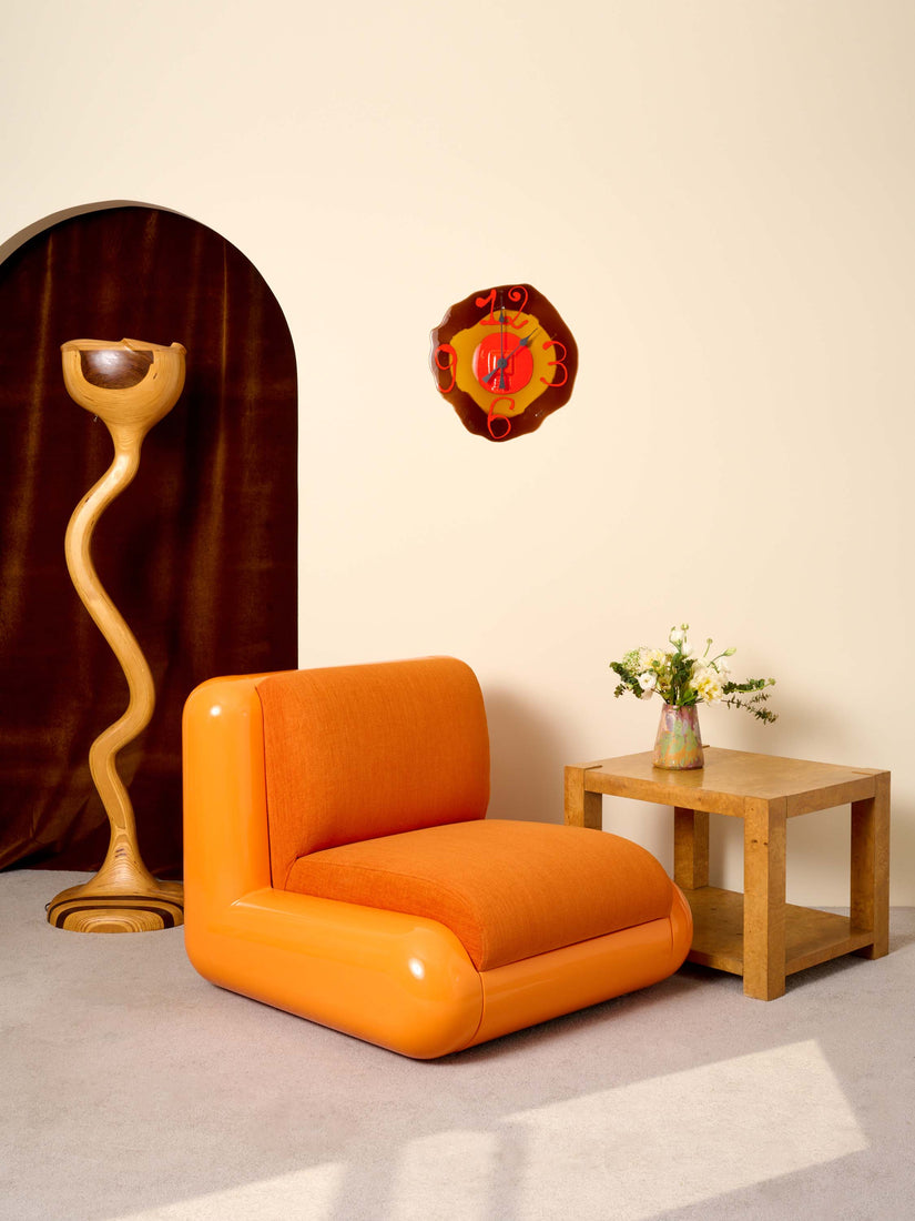An Uma T4 Chair in Orange styled with a sculptural wooden floor lamp, burl side table, and brown Watch Me Clock.