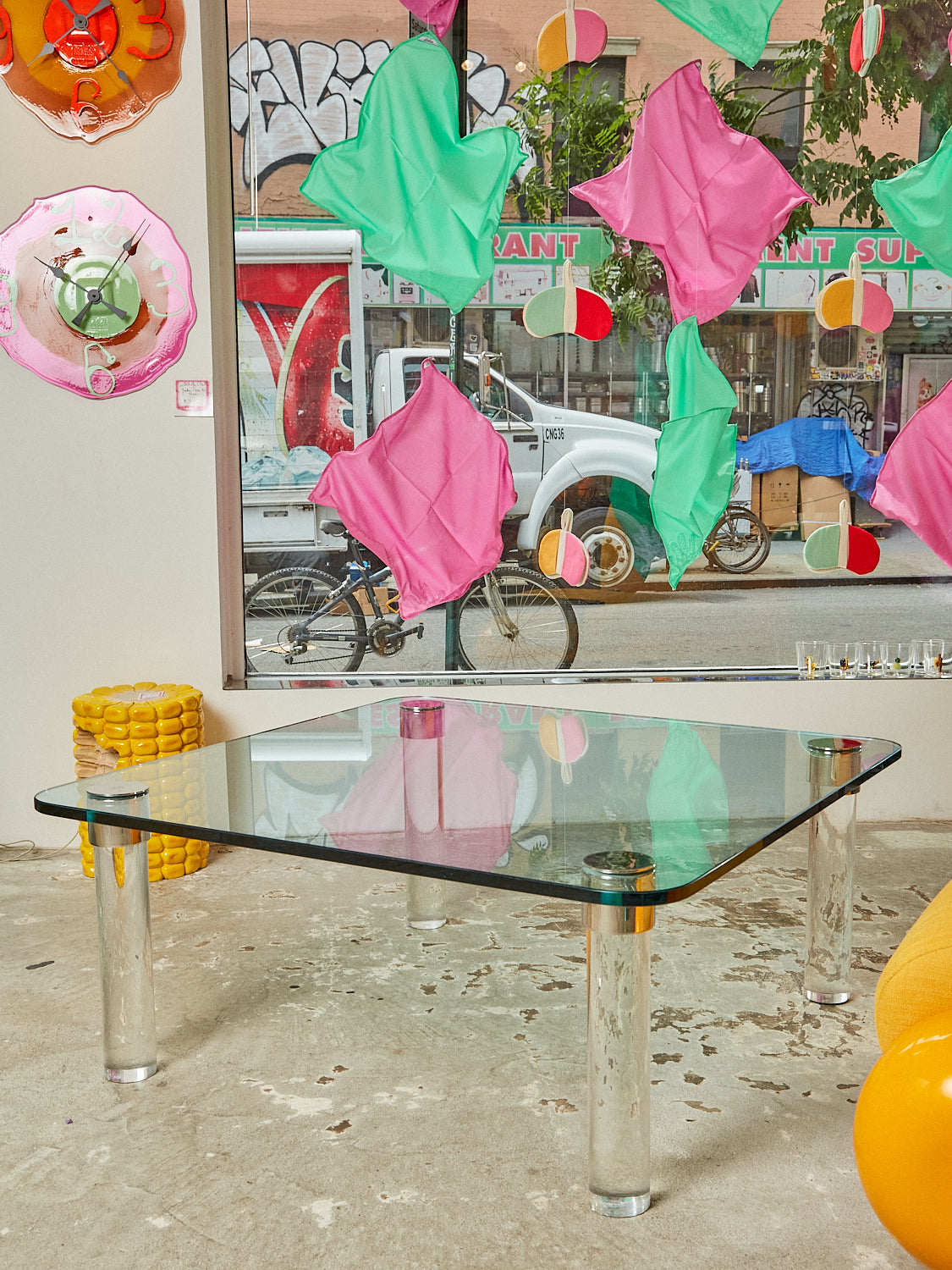 Square glass coffee table with lucite column legs and chrome hardware sitting in the Coming Soon store.