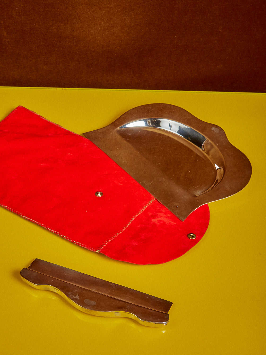 A Sterling Silver Crumb Catcher sits atop its red pouch on a yellow table top.