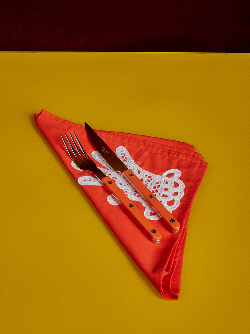 An orange dinner napkin paired with Sabre bistro fork and knife in orange.