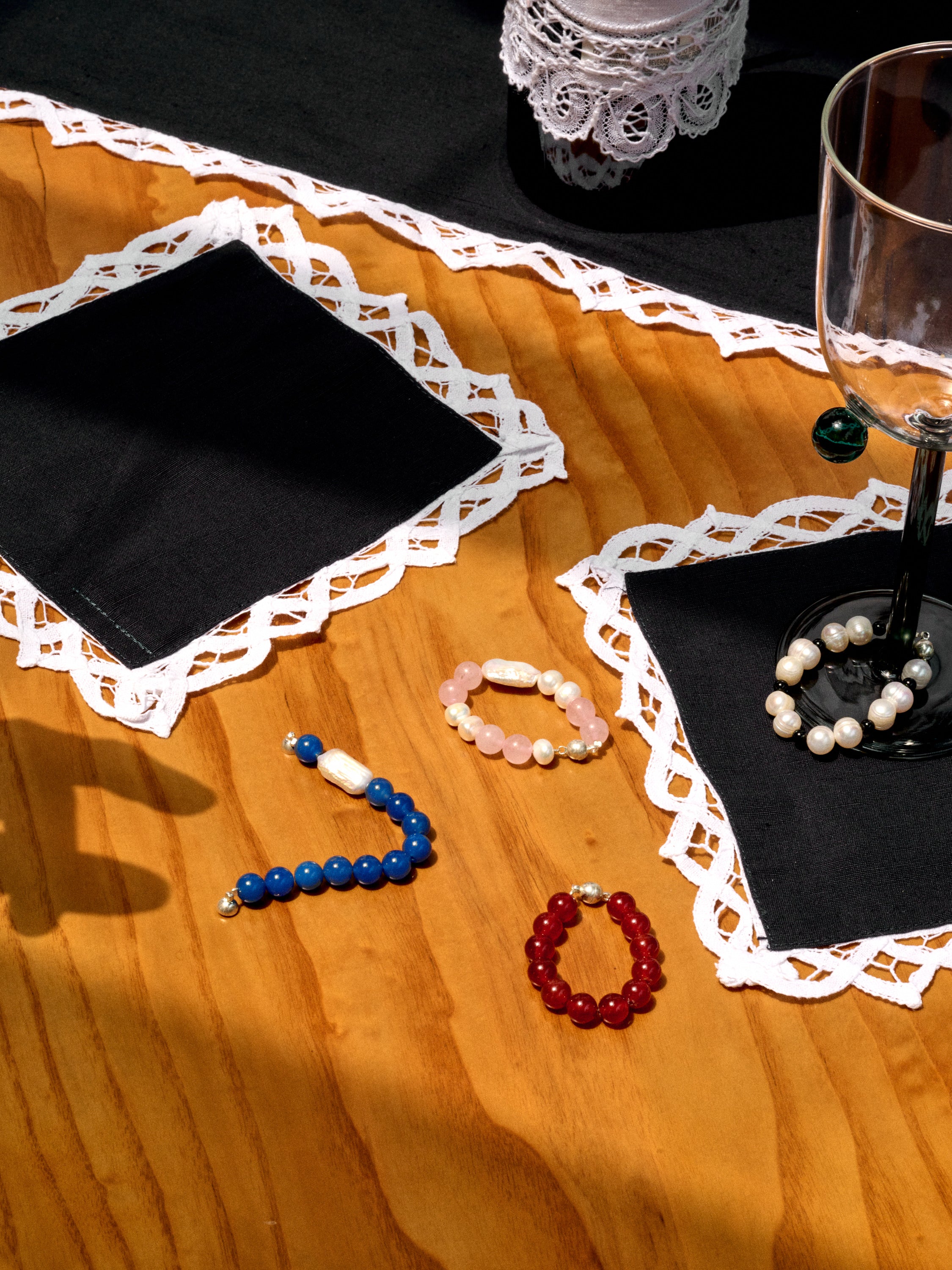 Bracelets for Stemware by Gohar World scattered across a wodden table with lace trim table linens, and a Pompom wine glass.