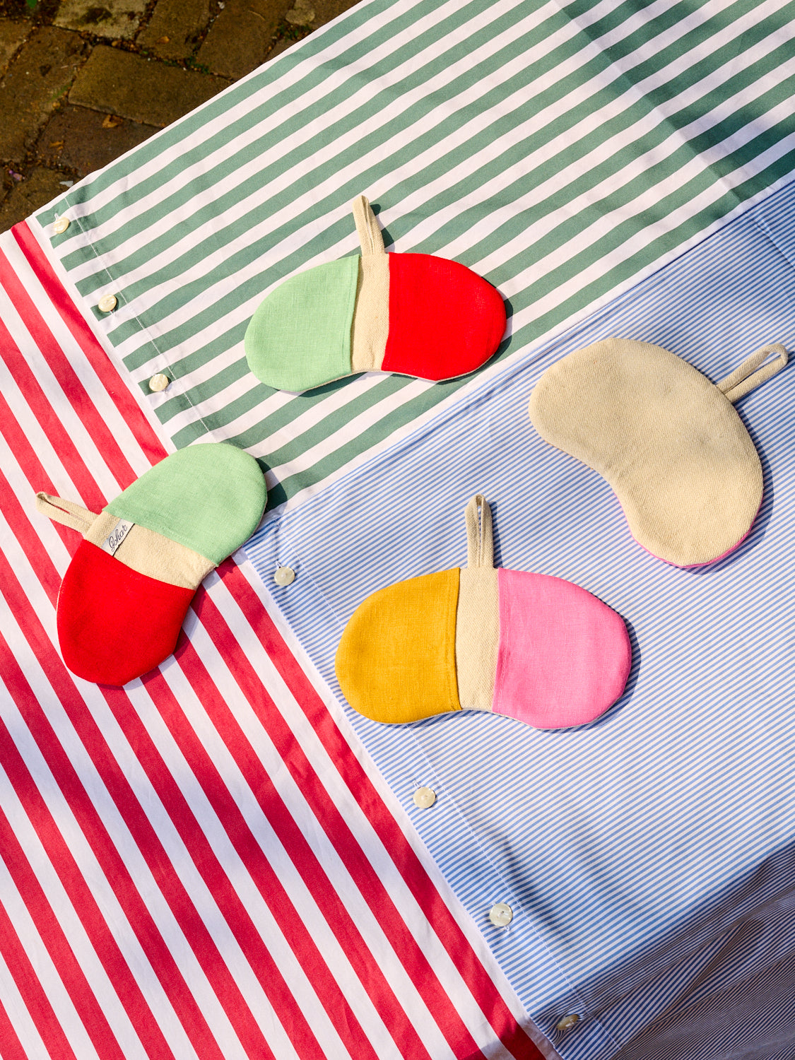 A pair of red/mint and orange/pink Bean Pot Mitts displayed on top of a Striped Table Cloth all by Gohar World.