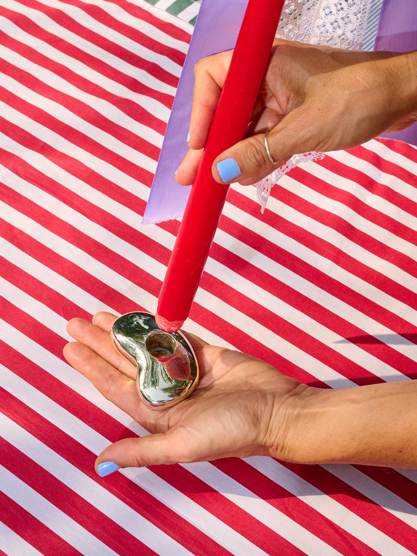 A hand cradles the Bean Candle Holder while the other hand places a red taper candle into it.