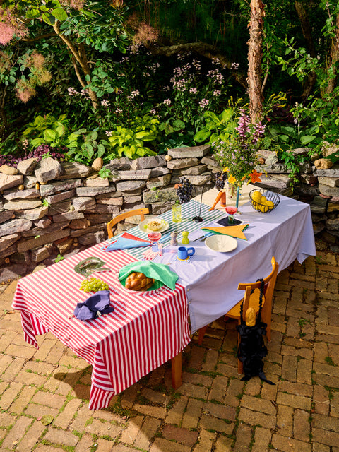 A full dinner spread on an outdoor table in a garden featuring a Stripe Tablecloth by Gohar World.