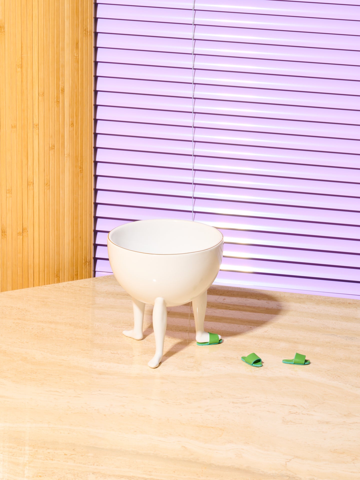 A three legged white ceramic bowl adorned with a gold rim and 3 green slides. The bowl wears 1 slipper and the other two slippers appear to be walking away.