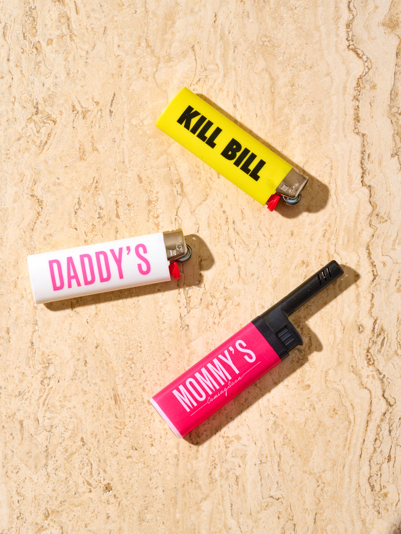 3 Coming Soon Lighters in different designs. A yellow lighter with black "KILL BILL" text, a white lighter with pink "DADDY'S" text, and a pink Bic Ez Reach lighter with white "MOMMY'S" text.