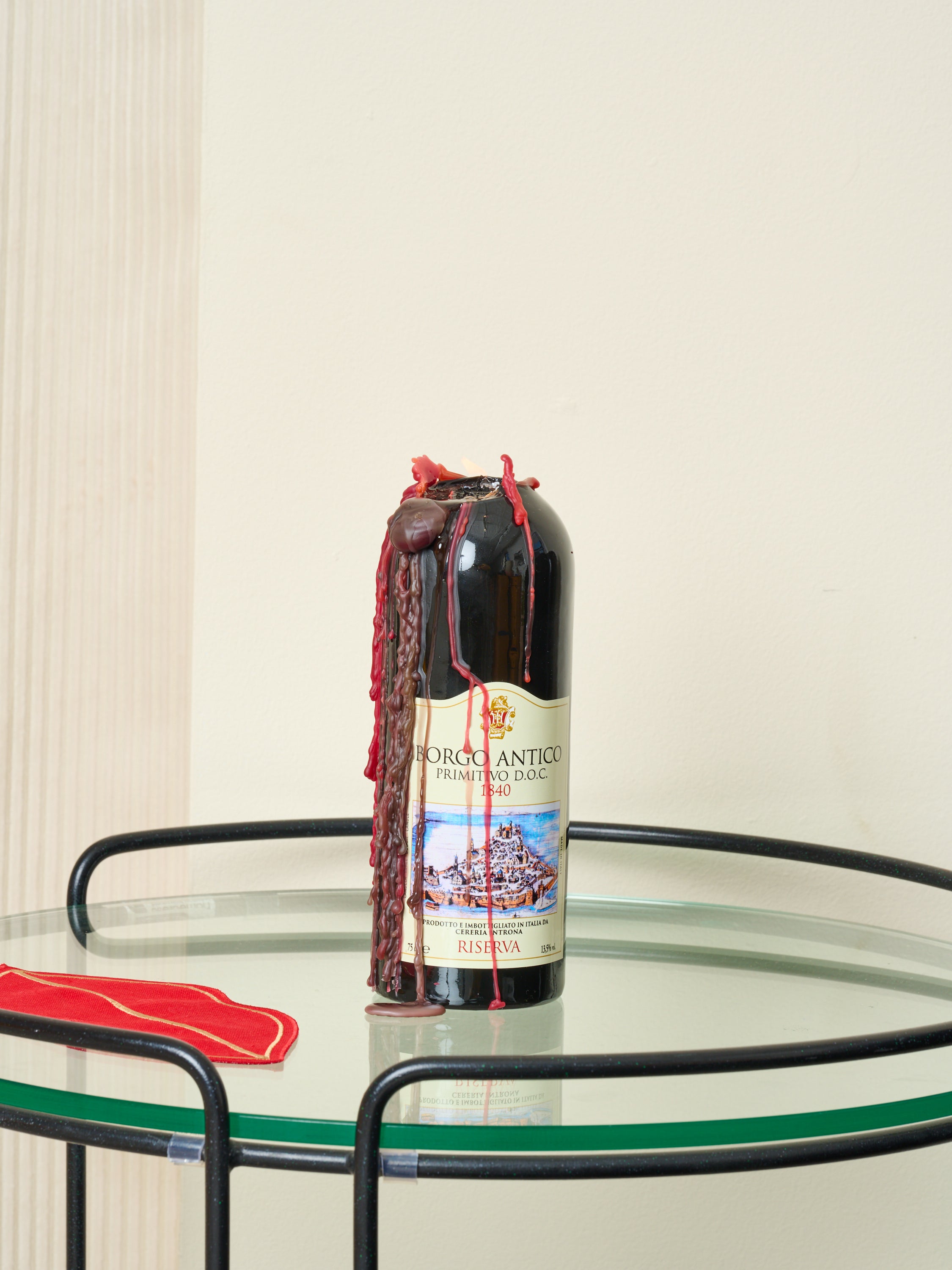 A Wine Bottle Candle by 54 Celcius sits on a glass side table, lit and melted down its stem.