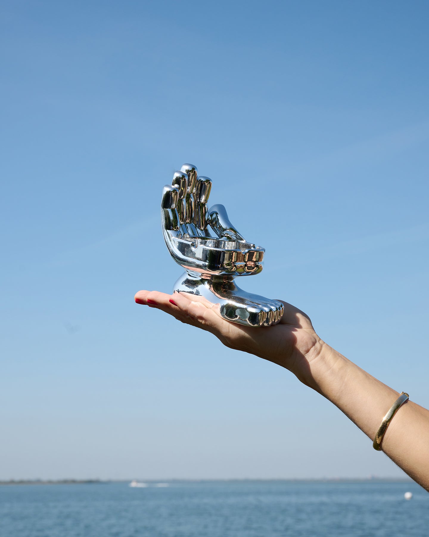 Hand and foot chrome astray is being held in the palm of someone's hand with the ocean and blue sky in the background.