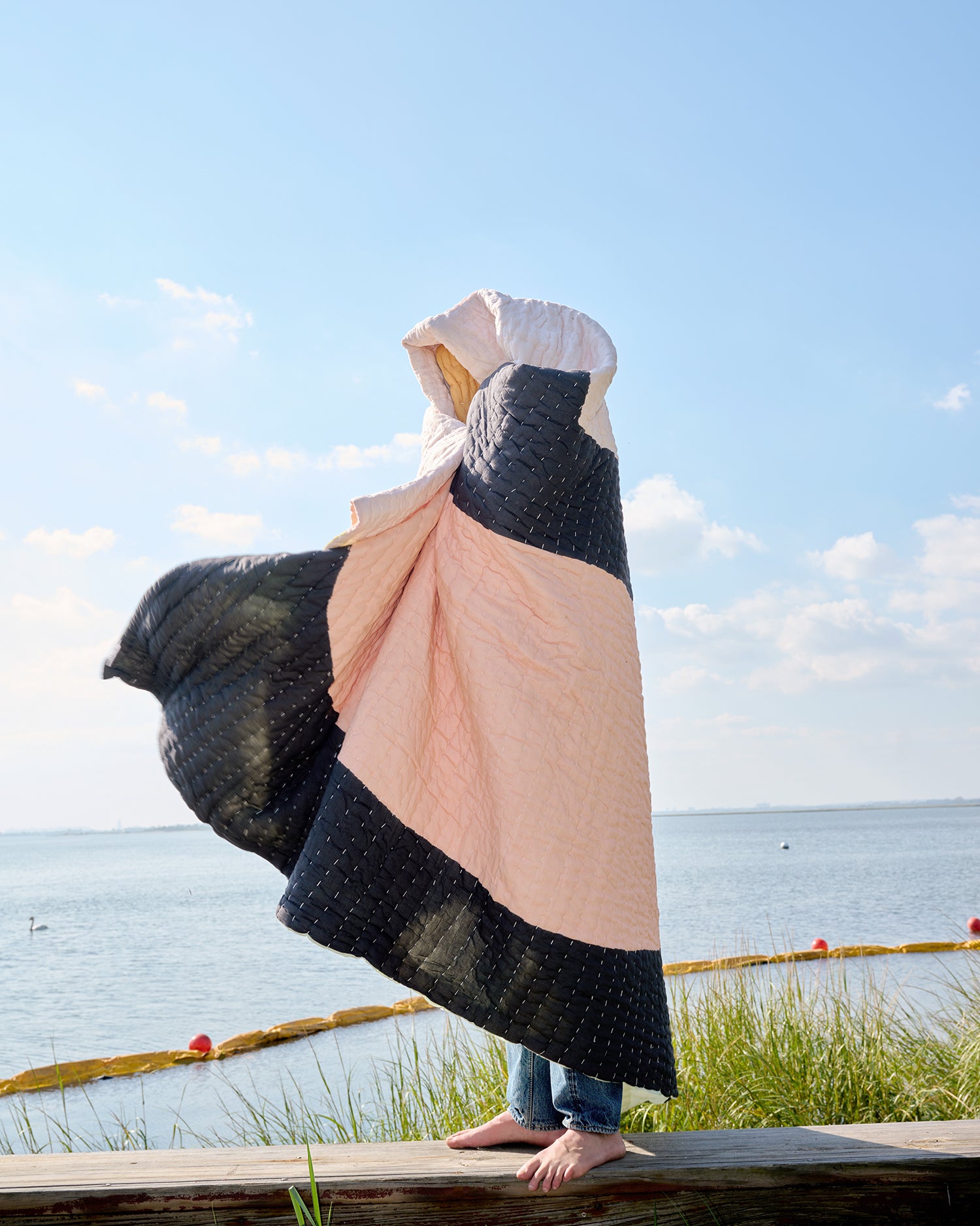 Someone stands on a dock wrapped up in a Summer is a Feeling Quilt by Cold Picnic.