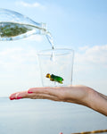 A small cup with a turtle figure made of glass sits in the palm of a person's hand. The turtle is green and yellow.