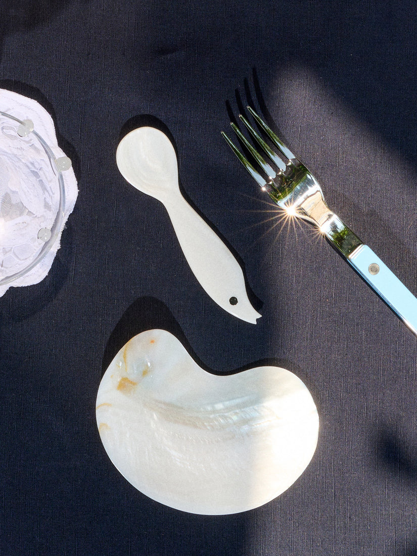 Sea Creature Spoon, Mother of Pearl Bean Dish, and a Sabre fork lay across a black table cloth