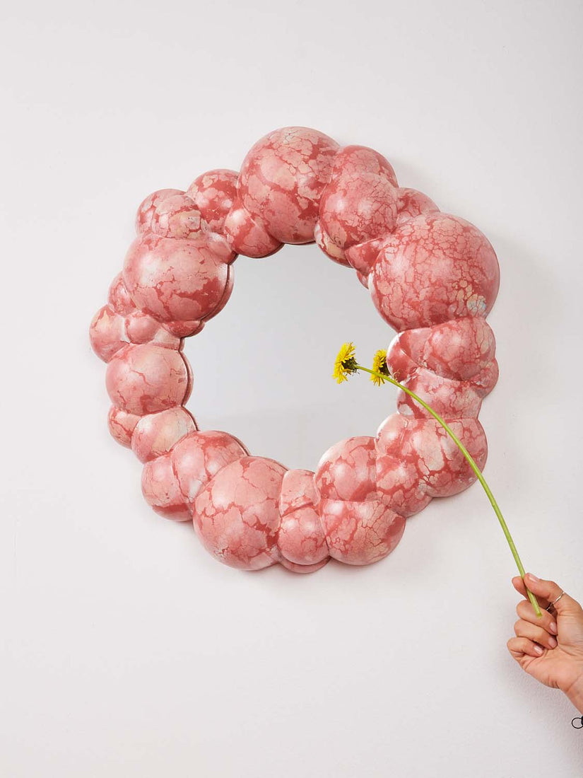 Bubble Mirror by Concrete Cat in pink red colorway. A hand holds a daisy in front of the mirror.