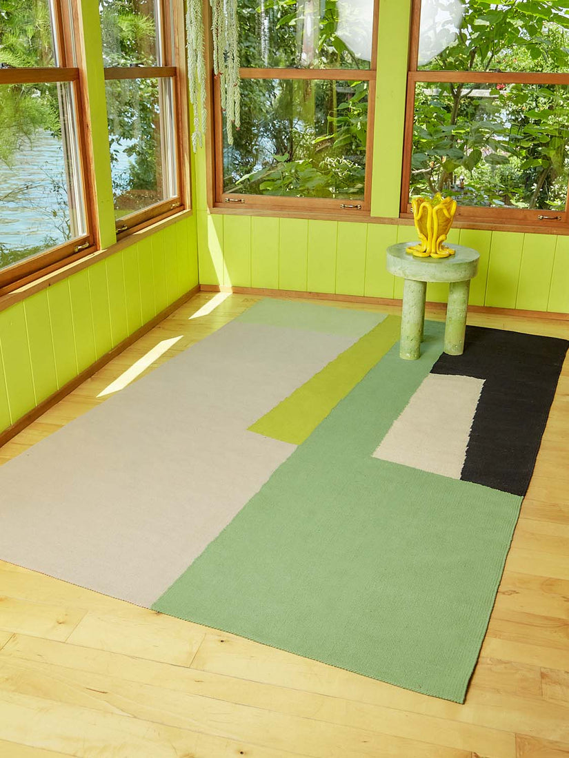 The Earthworm Rug in a sunroom with wooden floors and bright green walls.