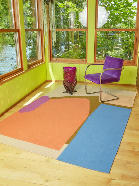 A woven rug by Cold Picnic with a purple velvet and chrome chair atop. A ruby red handmade resin vase sits next to the chair in this lime green room.