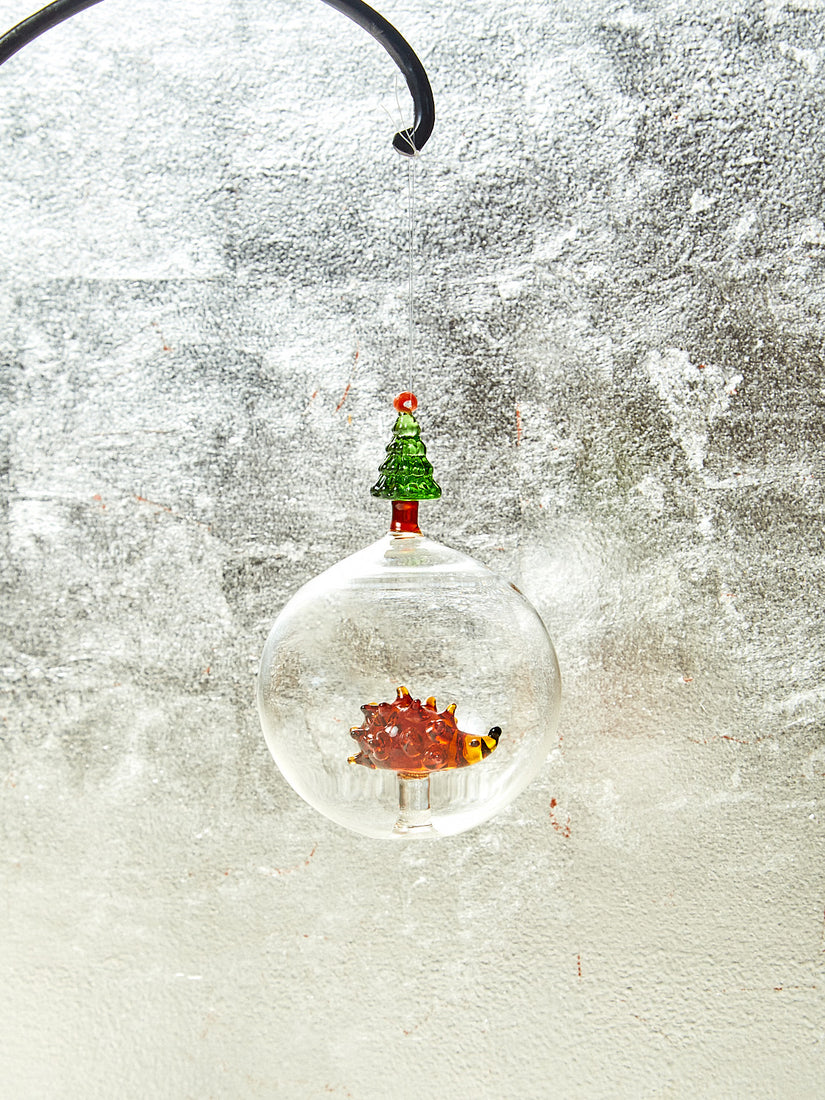 Glass ornament with hedgehog inside and green tree on top.