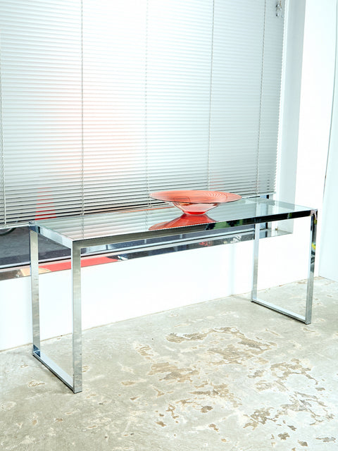 Vintage Chrome and Glass Console sits in a room on concrete. On top of the console there is a big clear amber bow displayed.