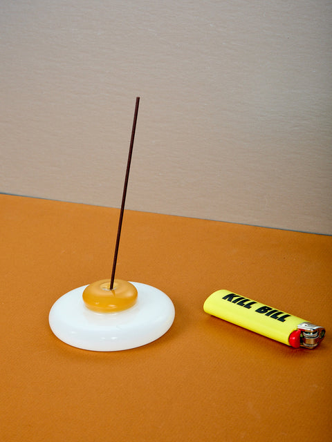 An egg shaped incense holder with incense next to a yellow lighter.