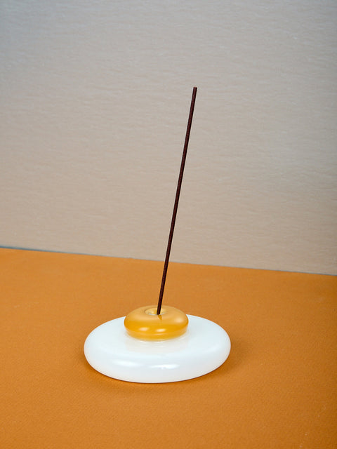 An egg shaped incense holder with a stick of incense.