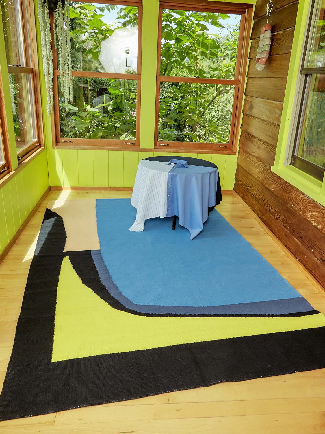 A round table wearing a Shirt Table Cloth sits atop the Lure a Wolf Rug by Cold Picnic.