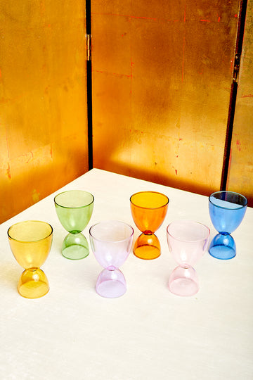 Six monotone cocktail glasses by Mamo in different colors. From left to right: honey, green, lavender, amber, pink, and blue.