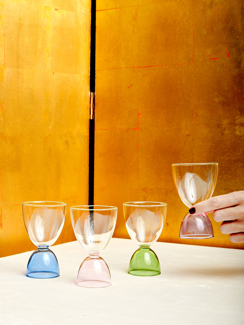 A hand holds up the lavender glass in a line of classic colorway cocktail glasses.