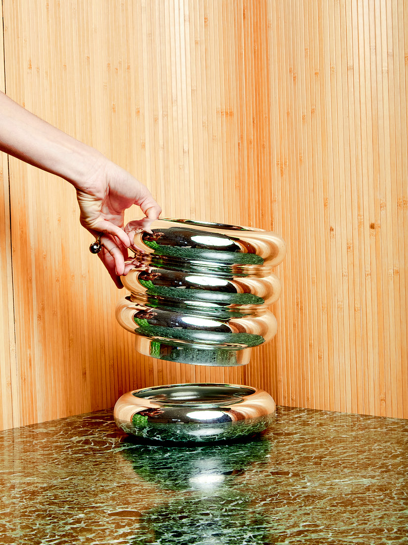 A hand holds the pot portion of the Chrome Stacking Planter up from its matching saucer.