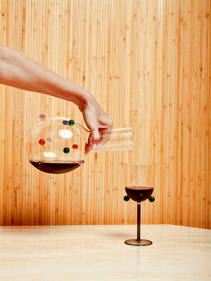 Someone out of frame pours red wine from a Dot Carafe into a Pompom Wine Glass by Maison Balzac.