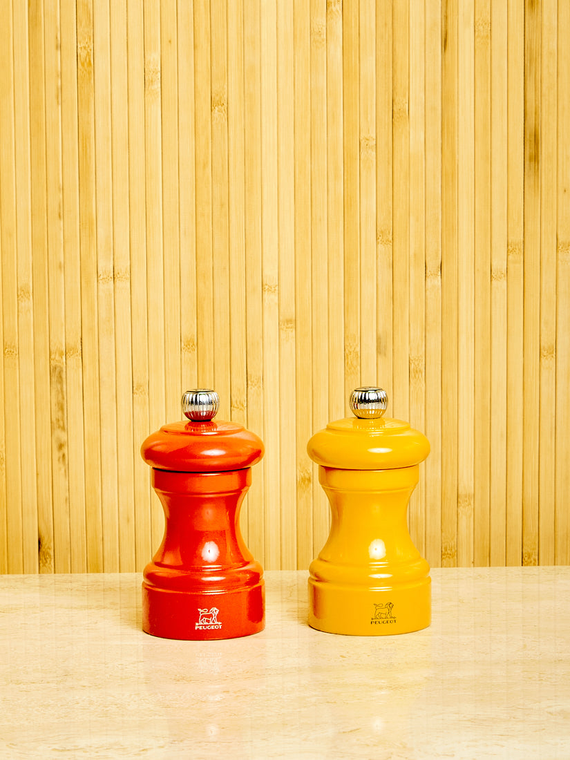 One orange and one yellow Salt and Pepper Mill by Peugeot.