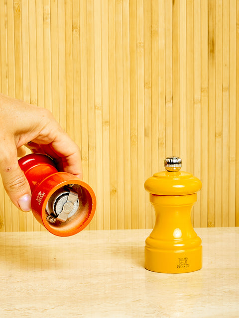 A hand holds up the orange mill from the orange and yellow Salt and Pepper Mill set by Peugeot.