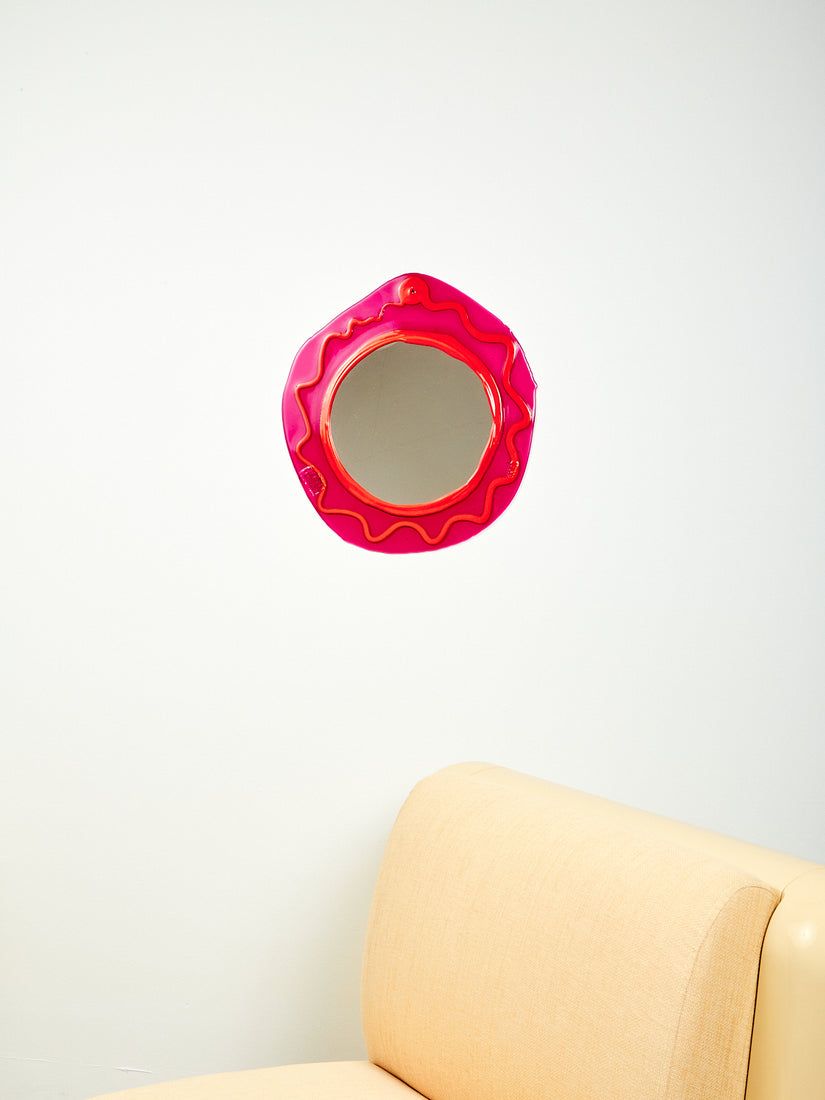 Round Mirror in Fuchsia Orange hung on a white wall above a cream Uma T4 chair.