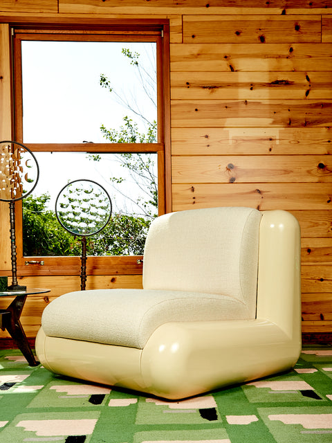 A Cream Boucle Uma T4 Chair in a green patterned carpeted room with wooden slat walls.