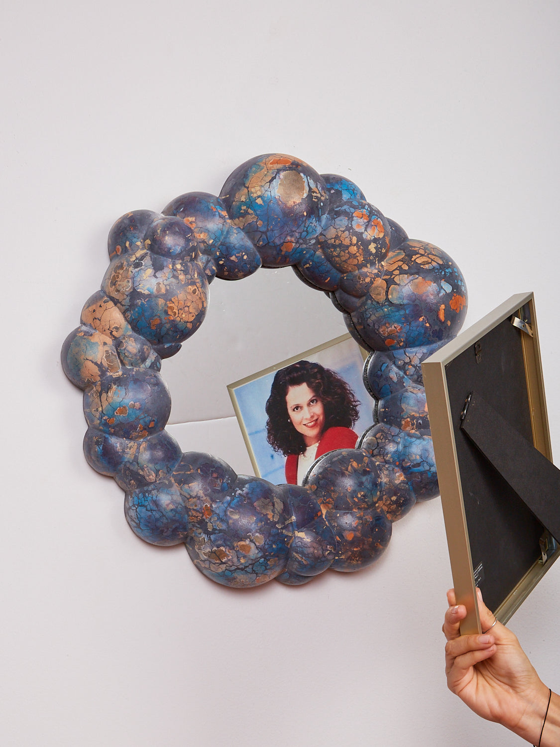 Someone holds a picture frame of Sigourney Weaver in front of the Bubble Mirror by Concrete Cat. 