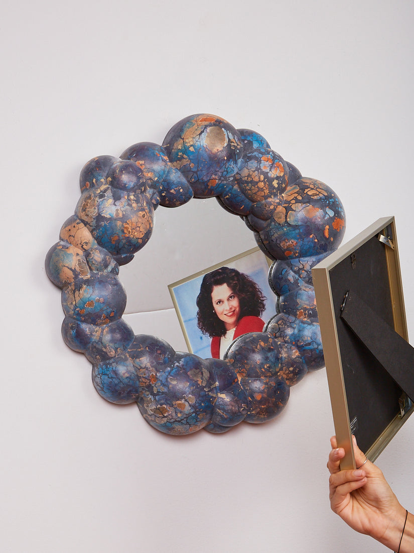 Someone holds a picture frame of Sigourney Weaver in front of the Bubble Mirror by Concrete Cat. 