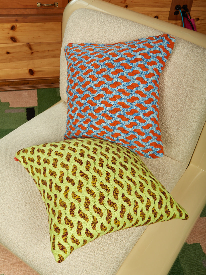 A blue and orange pillow, and lime and brown pillow on a white chair.