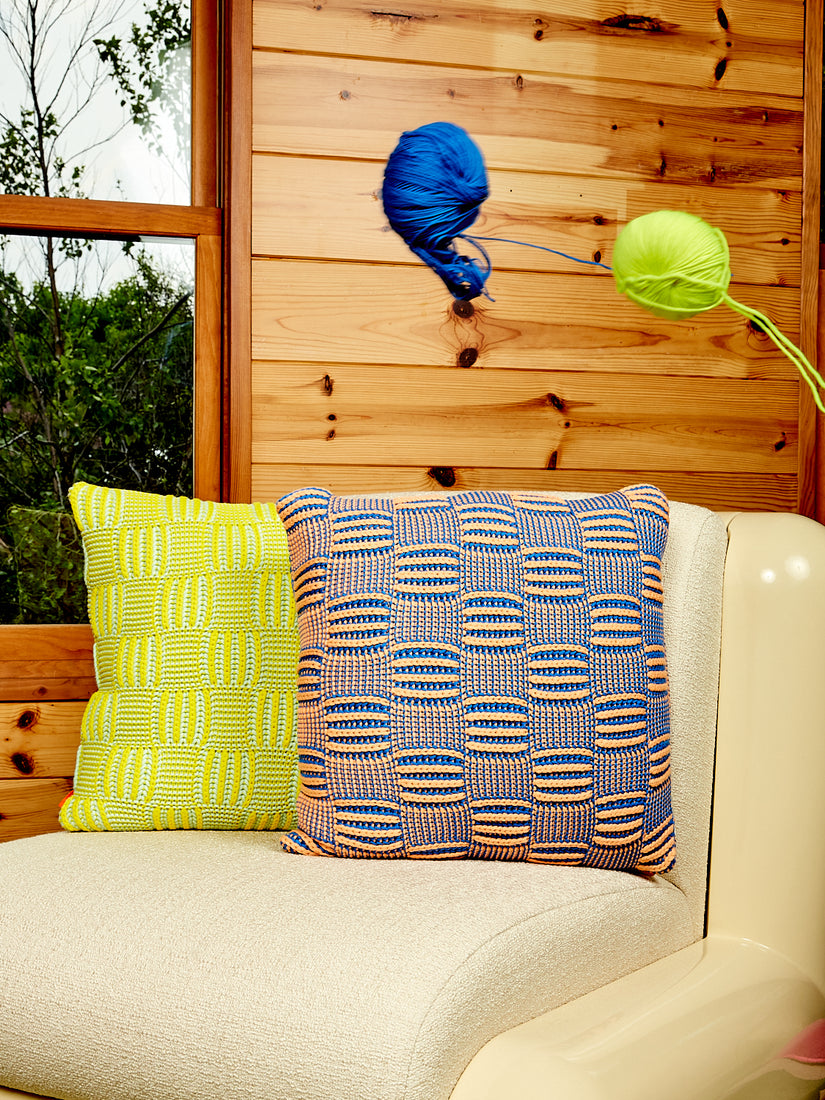 A ball of blue and ball of lime green yarn fly over a Uma T4 Chair with 2 chunky Chckerboard Pillows by Verloop.