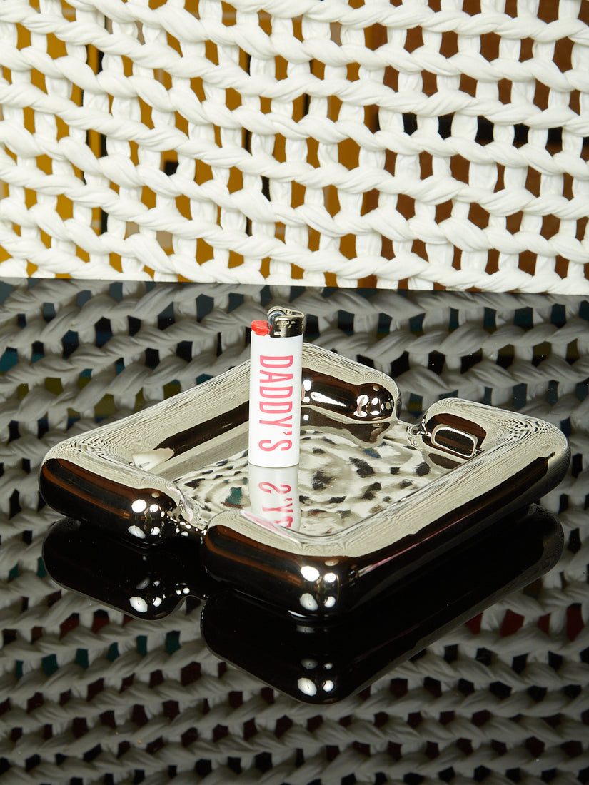 A white Coming Soon "Daddy's"  lighter sits atop a Hug Tray by Kouros.