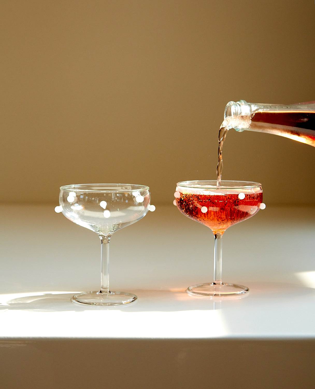 A bottle of lambrusco being poured into a pair of white dot coupes by Maison Balzac.