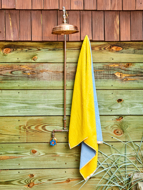 A yellow and cornflower bath towel hanging next to an outdoor shower.