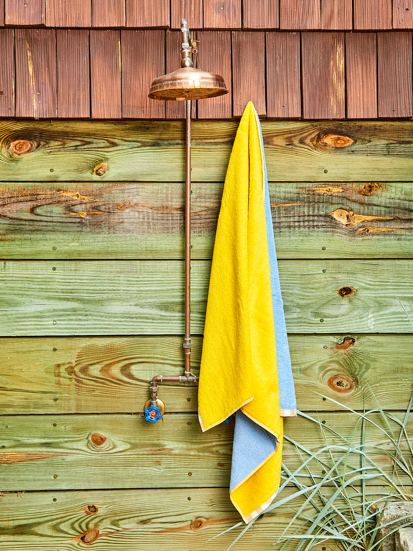 A yellow and cornflower bath towel hanging next to an outdoor shower.