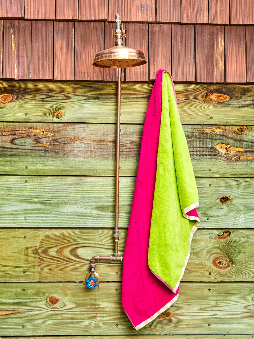 A magenta and green reversible bath towel hanging next to an outdoor shower.
