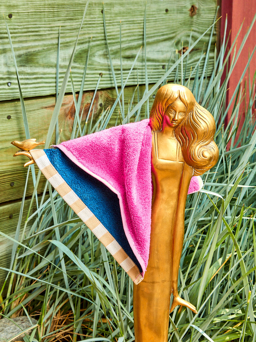 A pink and blue washcloth hanging on the arm of a brass woman sculpture outdoors.