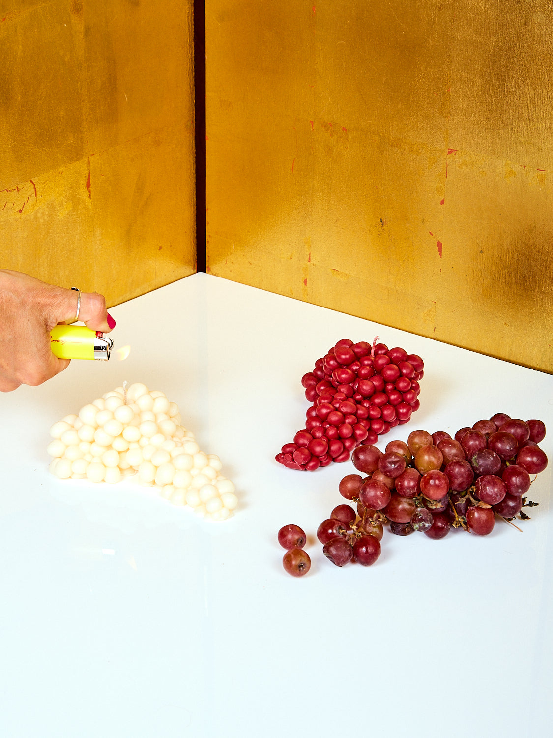 A white grape candle and wine grape candle sitting next to a bunch of real grapes.