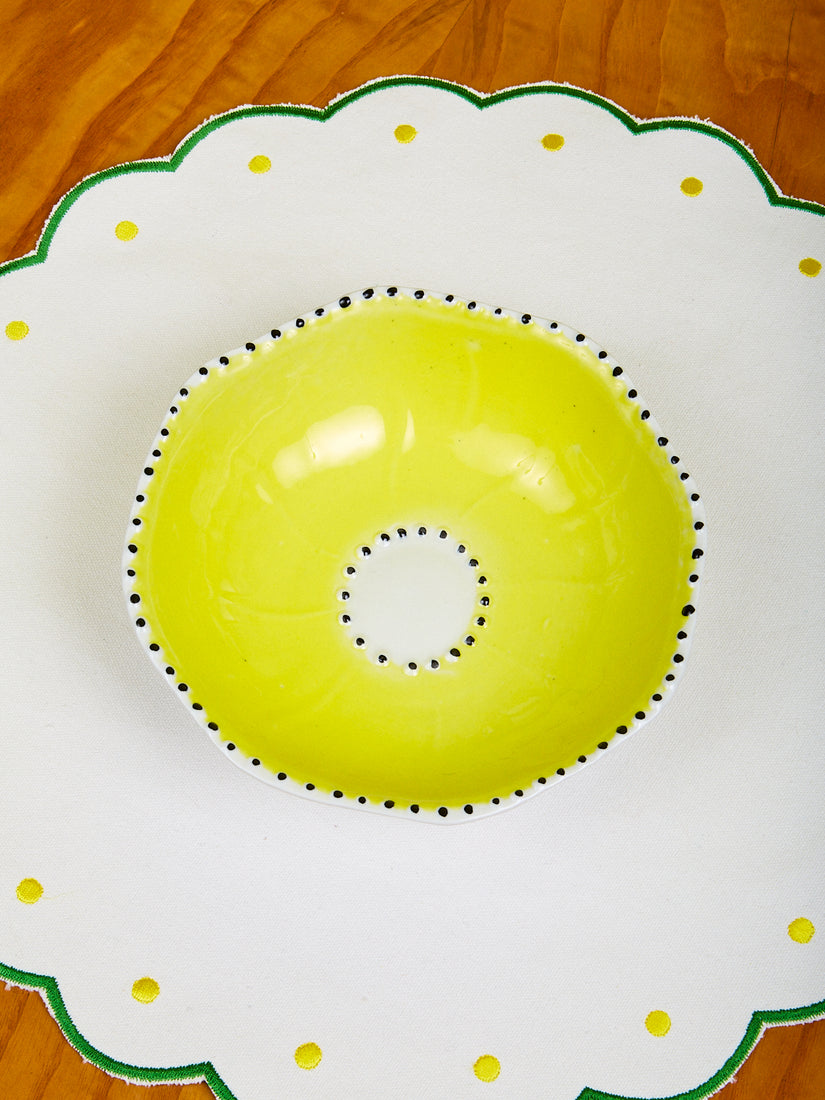 A Yellow Poppy Bowl by La Romaine Editions on a scalloped placemat.