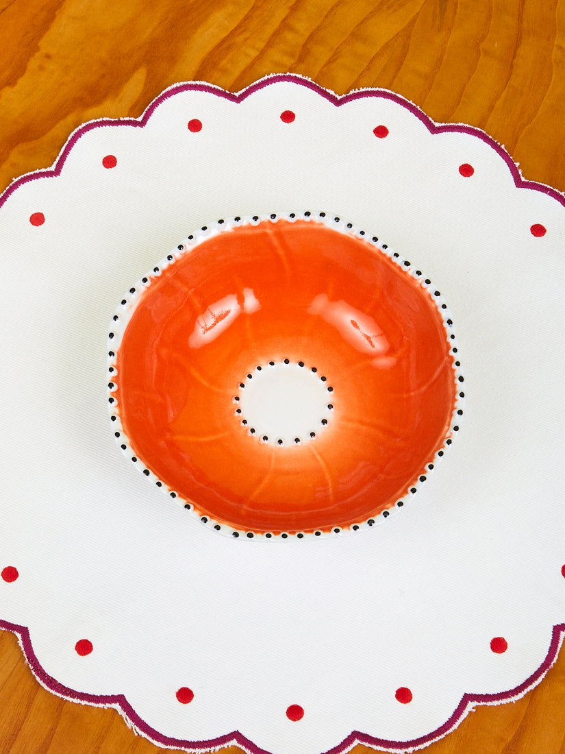 An Orange Poppy Bowl by La Romaine Editions on a scalloped placemat.