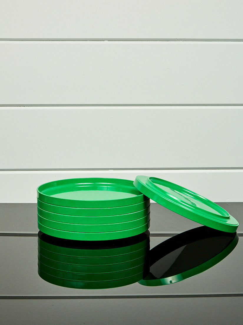 A stack of green dinner plates by Heller with one laying and leaning upside down.