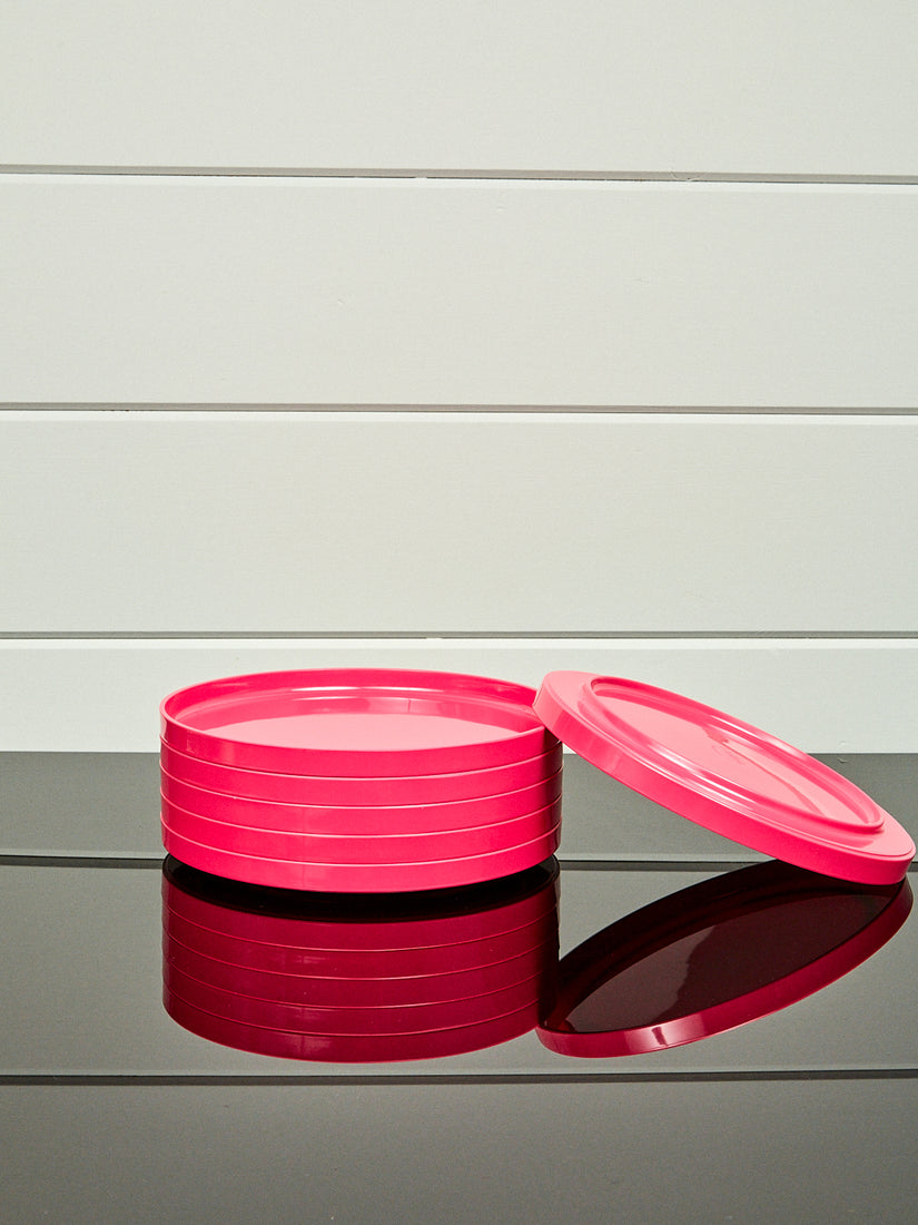 A stack of pink dinner plates by Heller with one laying and leaning upside down.