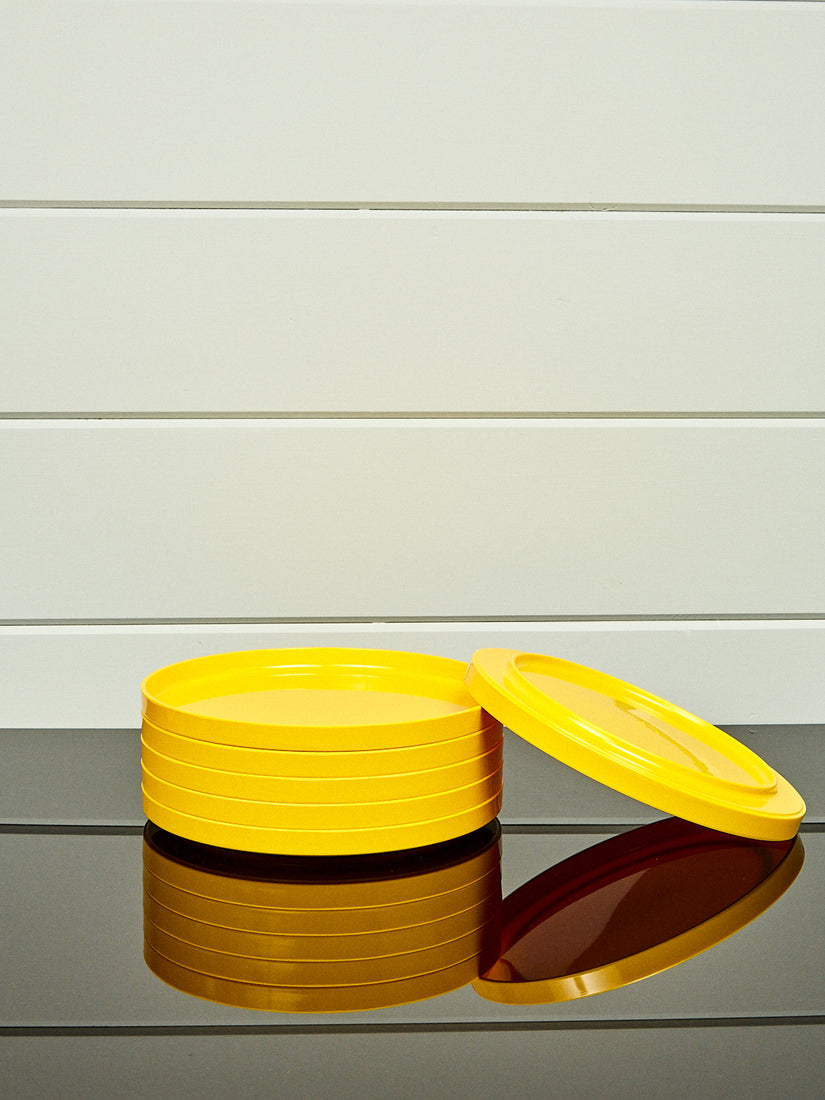 A stack of yellow dinner plates by Heller with one laying and leaning upside down.