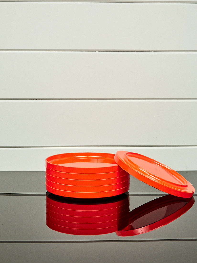 A stack of orange dinner plates by Heller with one laying and leaning upside down.